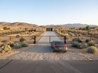 A closed steel driveway gate set far back from the street with a car parked on the driveway in front of it