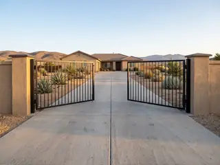 A black steel double swing driveway gate with both leaves open inward toward the house