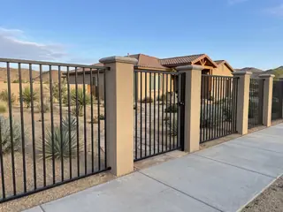 An open view steel front yard fence about shoulder high on stucco pillars, seen from the sidewalk