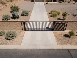 An elevated view of a closed black steel slide gate across a driveway, with its track running along the inside of a block wall