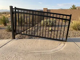 A sagging steel gate leaf dragging on the driveway, with a curved scrape mark on the concrete