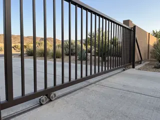 A closed dark bronze slide gate resting on grooved wheels in a steel track set in a concrete drive